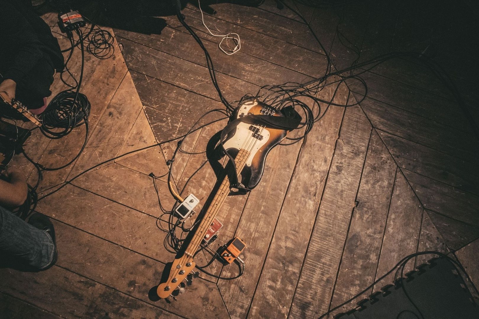 Elektrischer Bass mit Effektpedalen und Kabeln auf einer Holzbühne